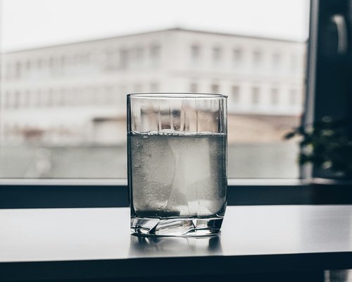 A glass of fresh water and a book on a table near a window